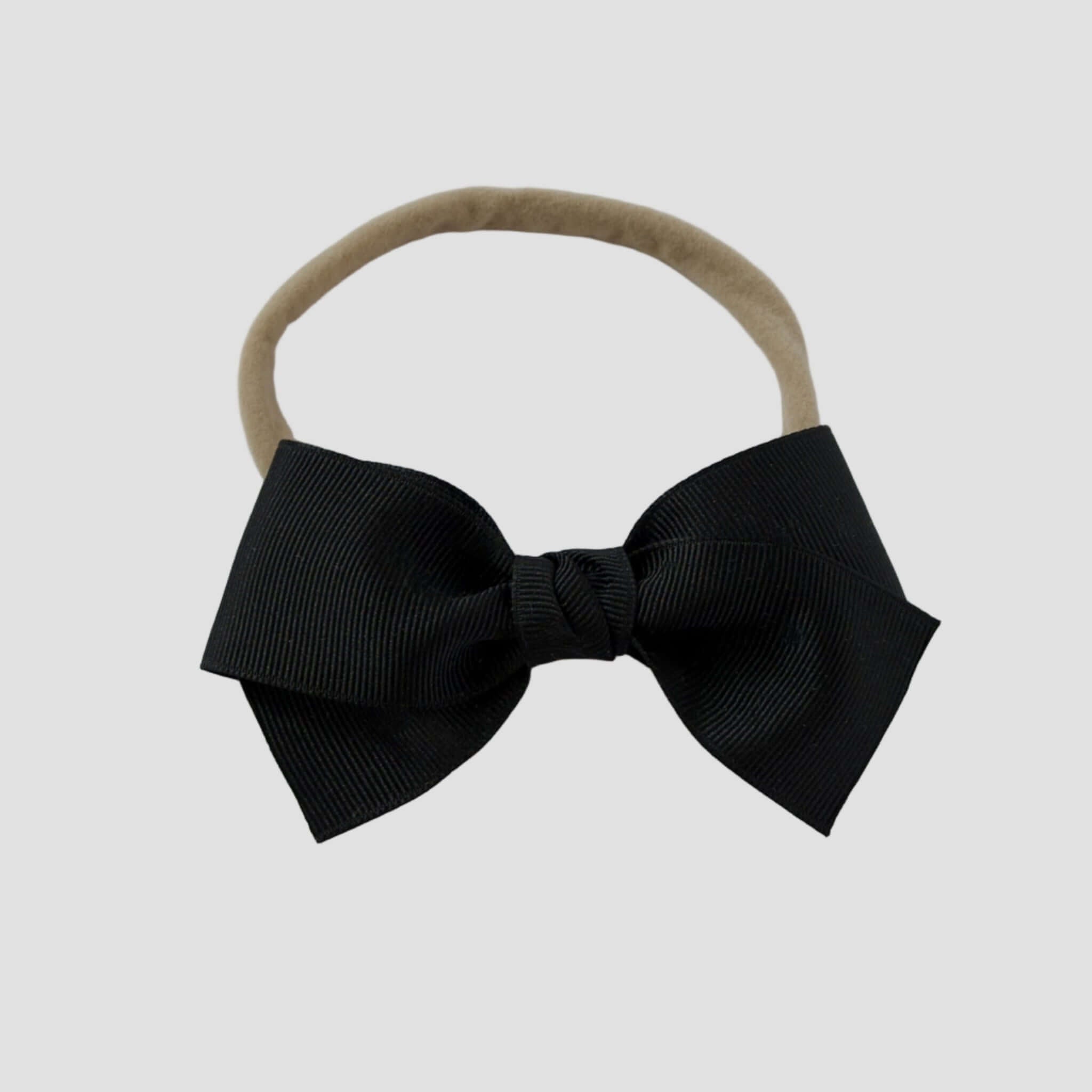 Black grosgrain Kayla hair bow on a nude nylon headband against a white background