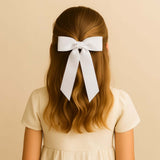 Girl with long hair wearing a large white grosgrain Zoe petite hair bow, against a beige background