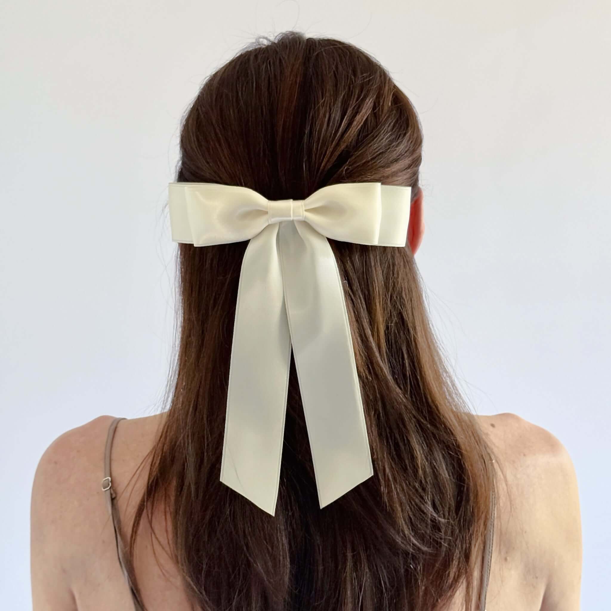 Model with long brown hair wearing a Grace satin bow in ivory bow against a white background
