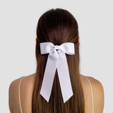 White hair bow on a person with long brown hair against a plain background