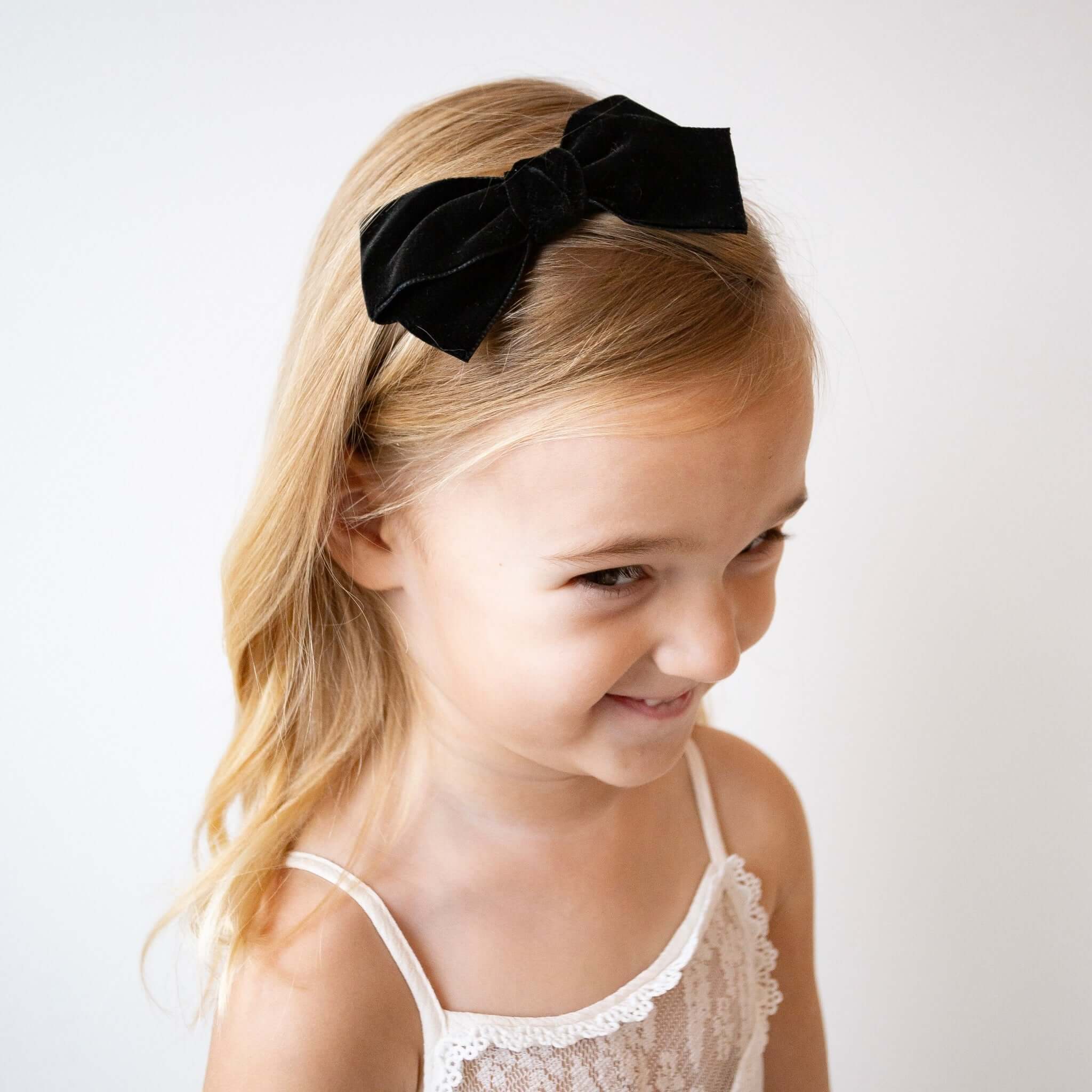 Young girl wearing a black velvet bow headband on a white background