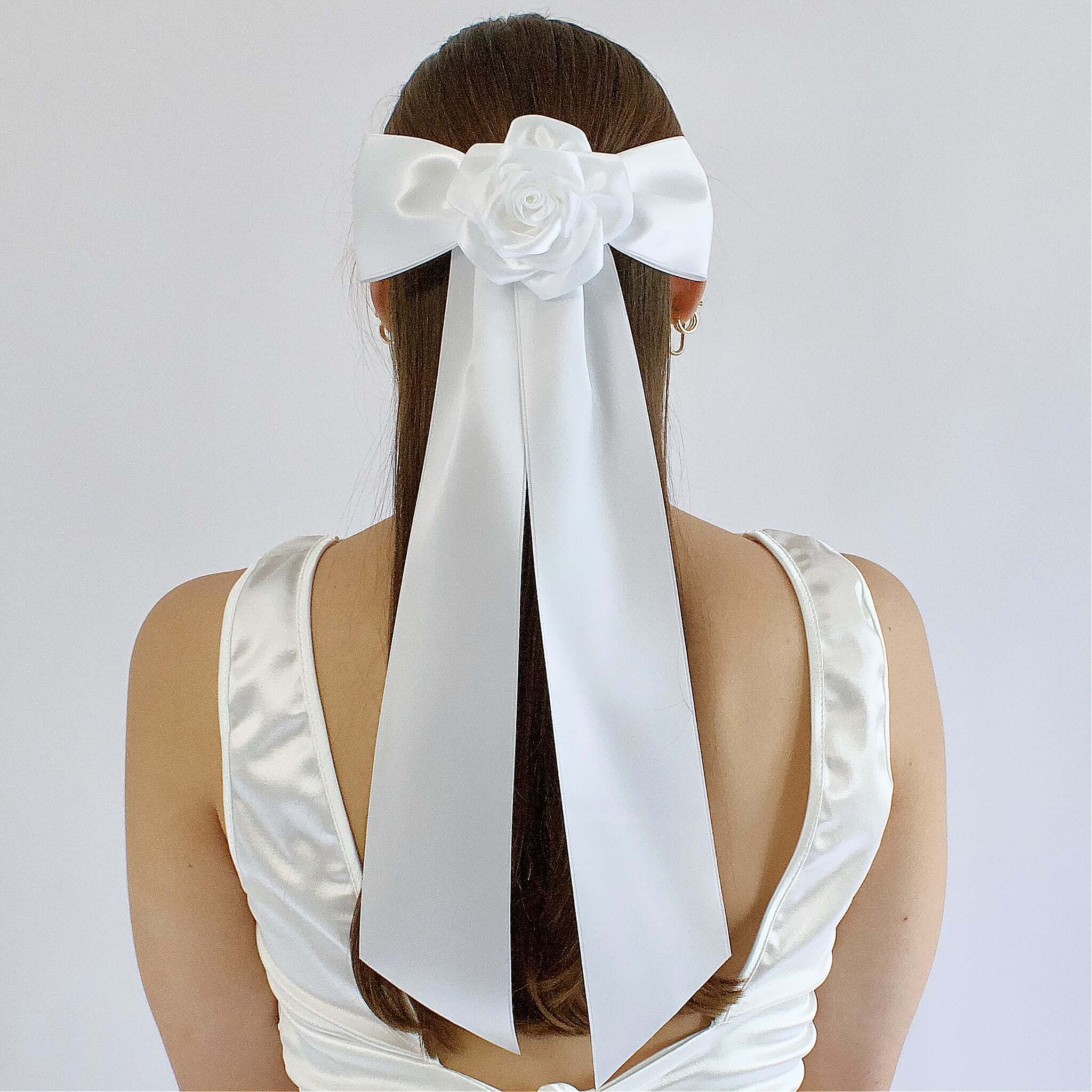 Woman wearing oversized white satin Zoe bow with flower, styled for bridal hair