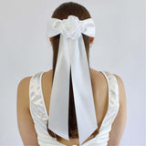 Woman wearing oversized white satin Zoe bow with flower, styled for bridal hair