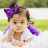 Baby with a purple bow and tutu sitting on grass