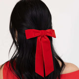 Woman with long black hair tied back with a large red velvet bow, conveying a festive and elegant tone. Chic & Effortless Ways to Style Your Hair with Bows