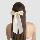 A woman with long brown hair wears a large ivory-colored bow at the back of her head, highlighting elegance and femininity. Bridal Hair Accessories Guide for Every Wedding Event.