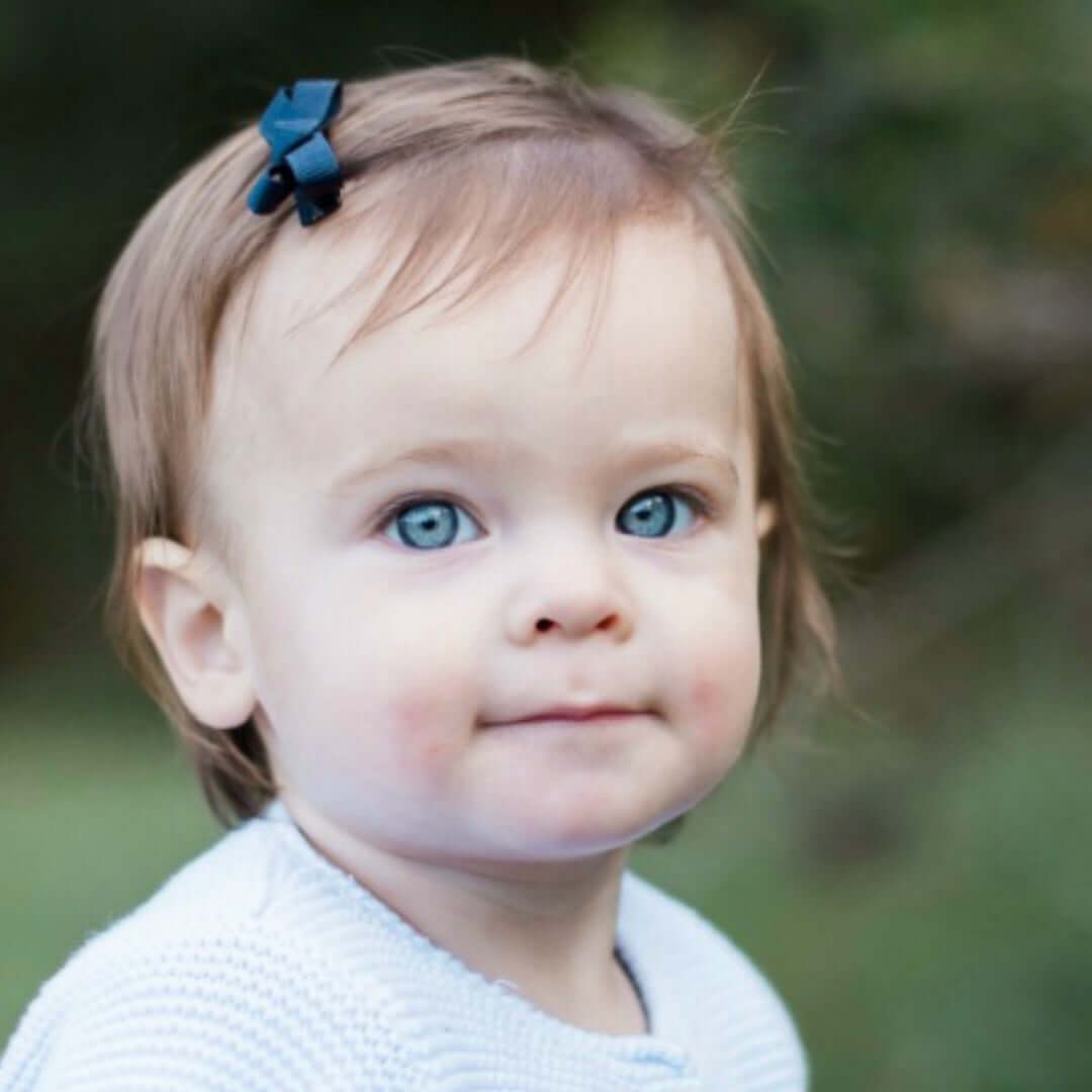Adorable baby girl with blue eyes wearing a mini grosgrain bow in her hair, featuring a secure snap clip with no-slip grip in pastel colors