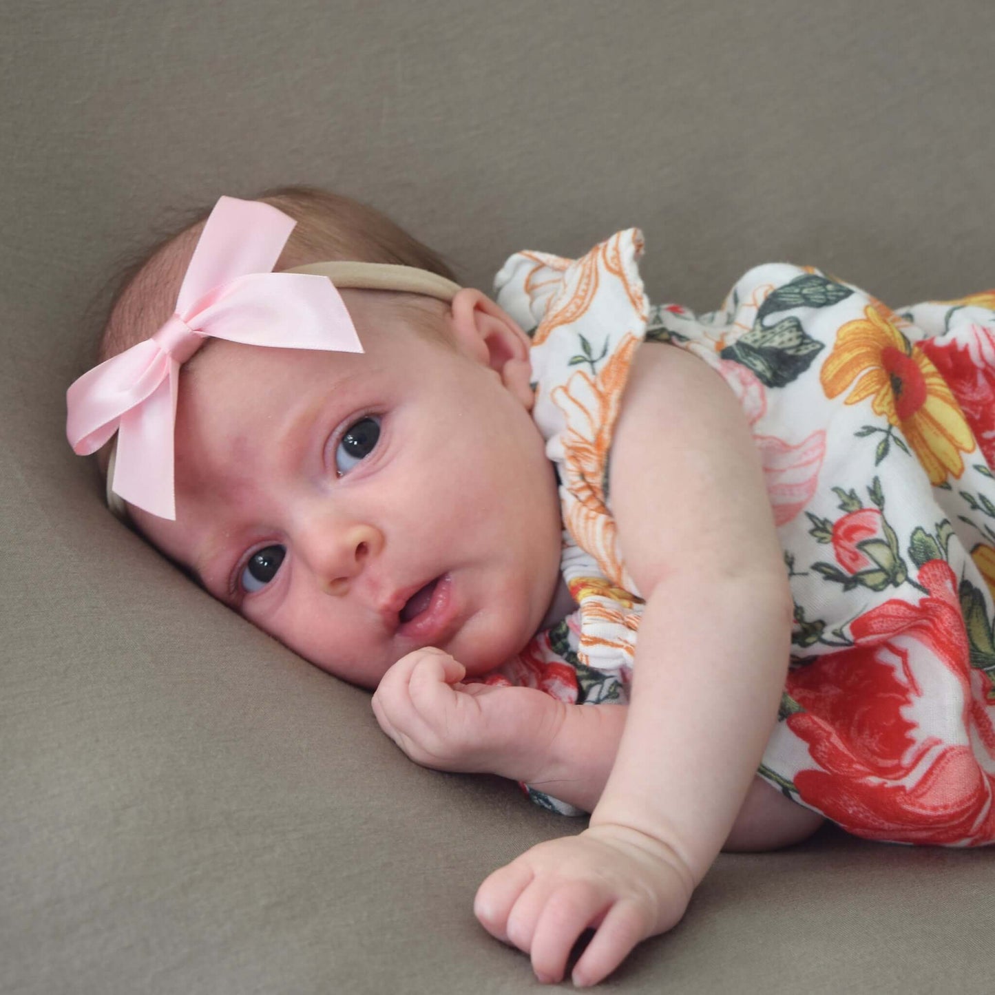 Baby wearing floral dress and pink grosgrain sailor bow headband lies on taupe background
