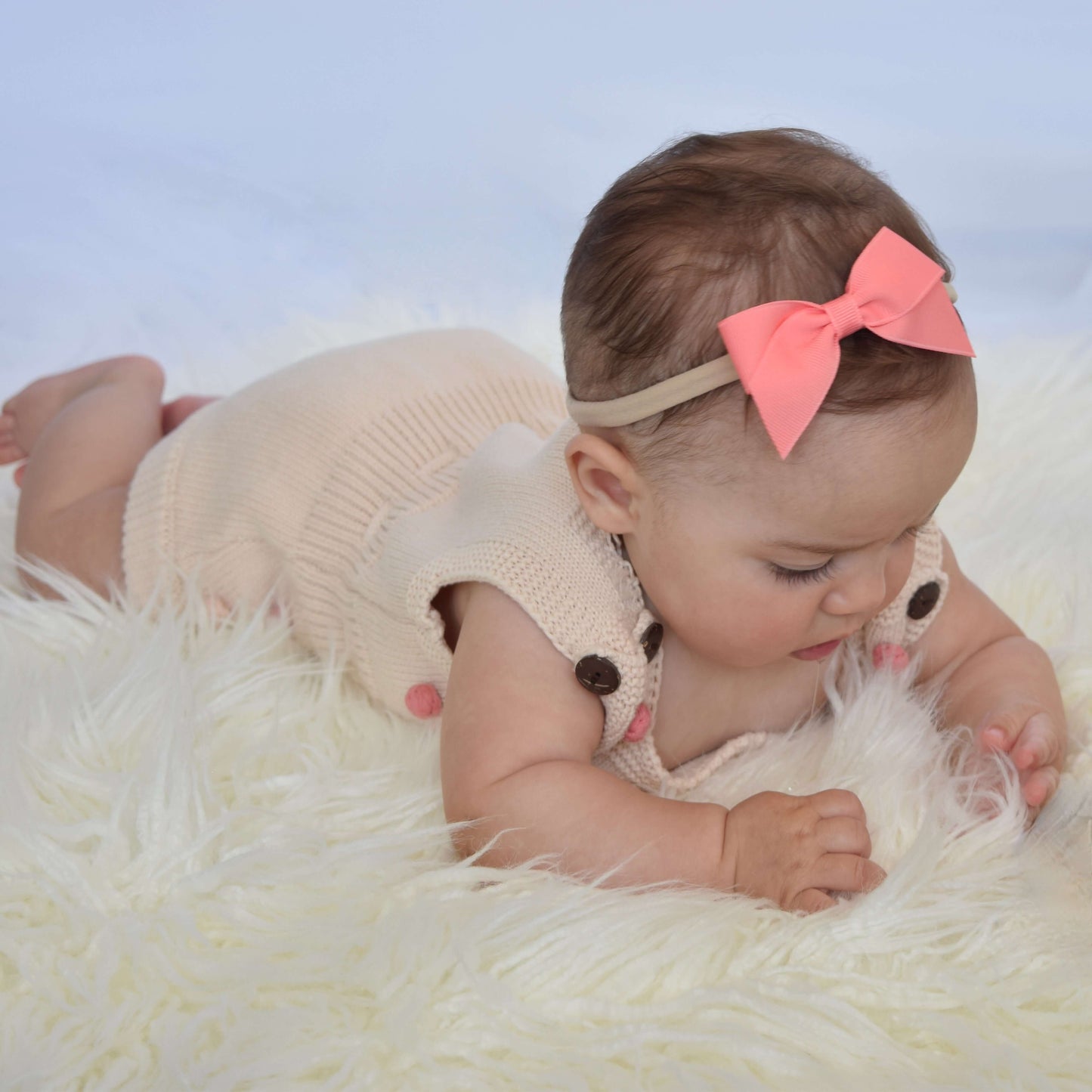 Baby wearing a pink grosgrain bow headband while lying on a fluffy white rug