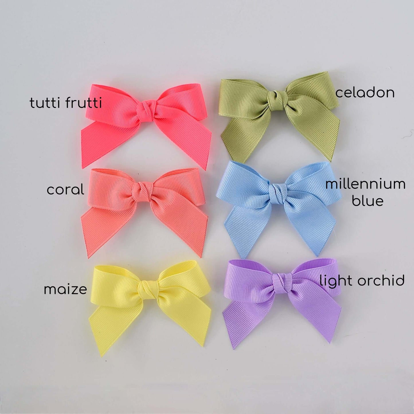 Six pastel-colored grosgrain Sailor bow clips in tutti frutti, celadon, coral, millennium blue, maize, and light orchid arranged together.