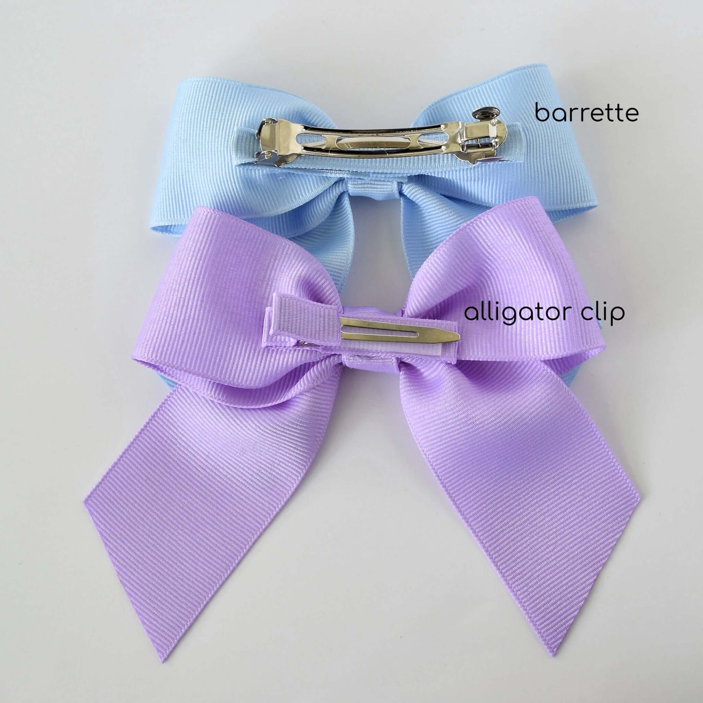 Light blue grosgrain sailor bow with French barrette and lavender grosgrain sailor bow with alligator clip, highlighting no-slip grip features.