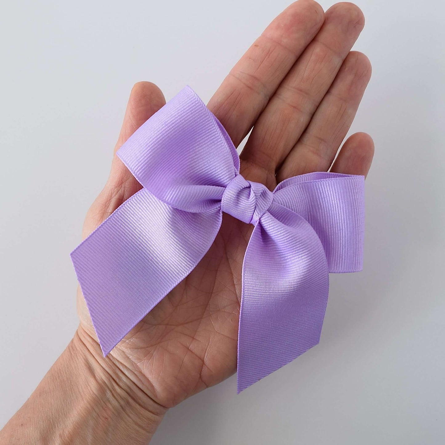 Hand holding pastel lavender 4 inch grosgrain sailor bow with alligator clip - perfect hair accessory for little girls.