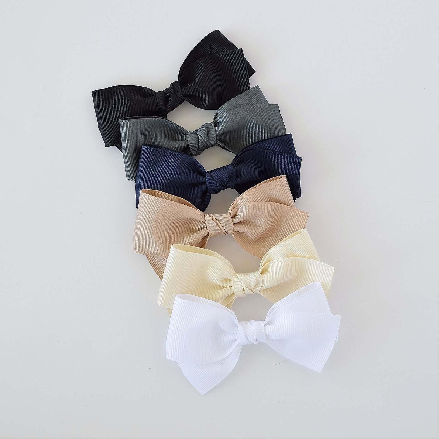 Six 4-inch grosgrain baby Kayla bow clips in black, gray, navy, taupe, ivory, and white. Versatile hair accessories for girls of any age.