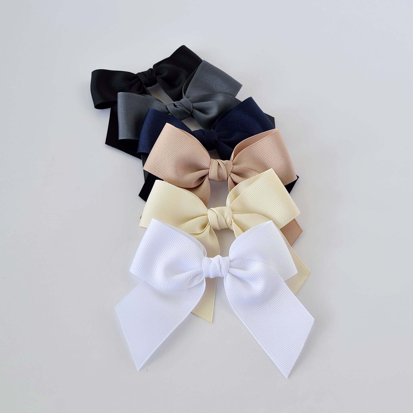 Neutral grosgrain sailor bows for toddlers and girls in black, navy, gray, taupe, ivory, and white arranged in a row.