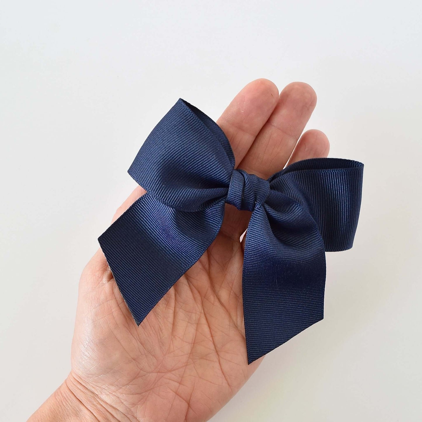 Hand holding a navy grosgrain sailor bow in neutral tones for toddlers and girls. Stylish hair accessory available with alligator clip or barrette.