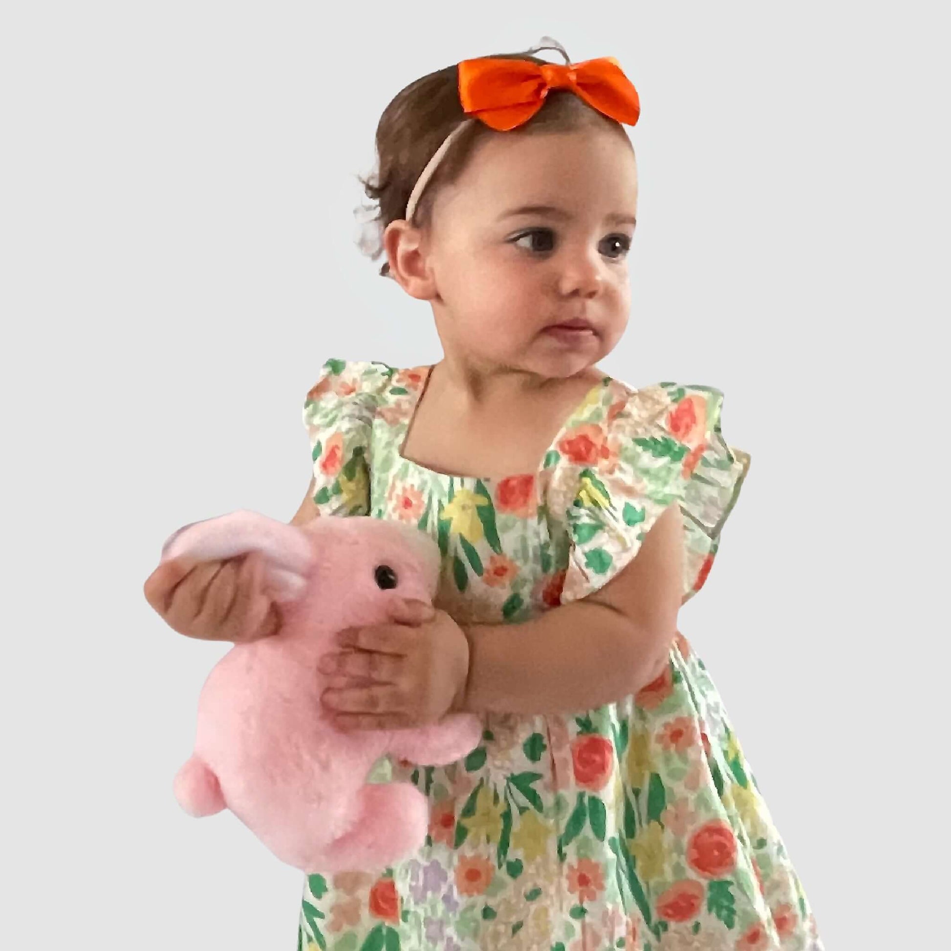Toddler girl in floral dress with orange grosgrain bow headband holding a pink stuffed bunny