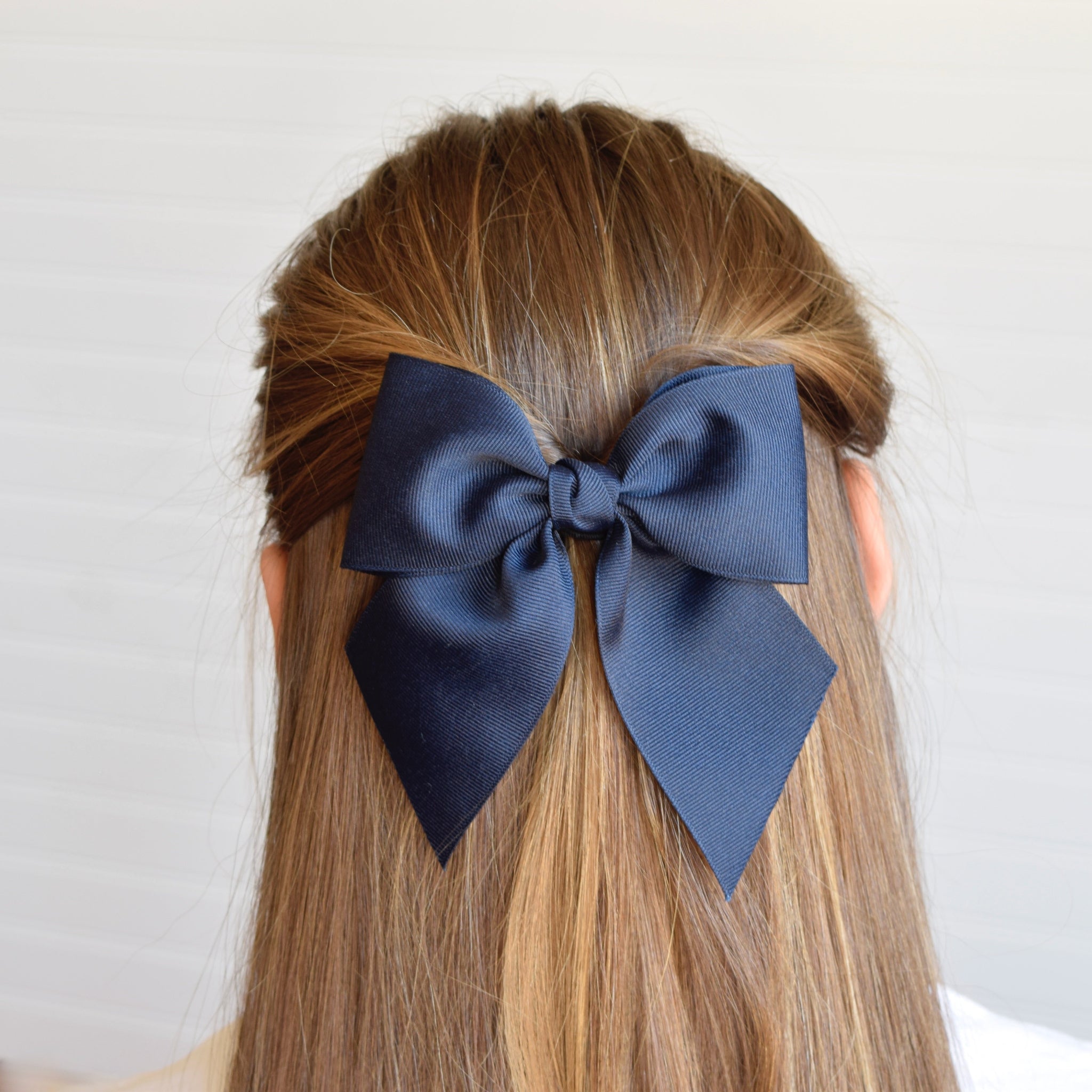 Adult wearing navy blue 5 inch sailor hair bow in a half-up twisted hairstyle against a white background