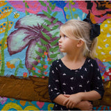 Young girl with a black 5 inch Penelope grosgrain bow in her hair standing in front of a colorful floral mural.