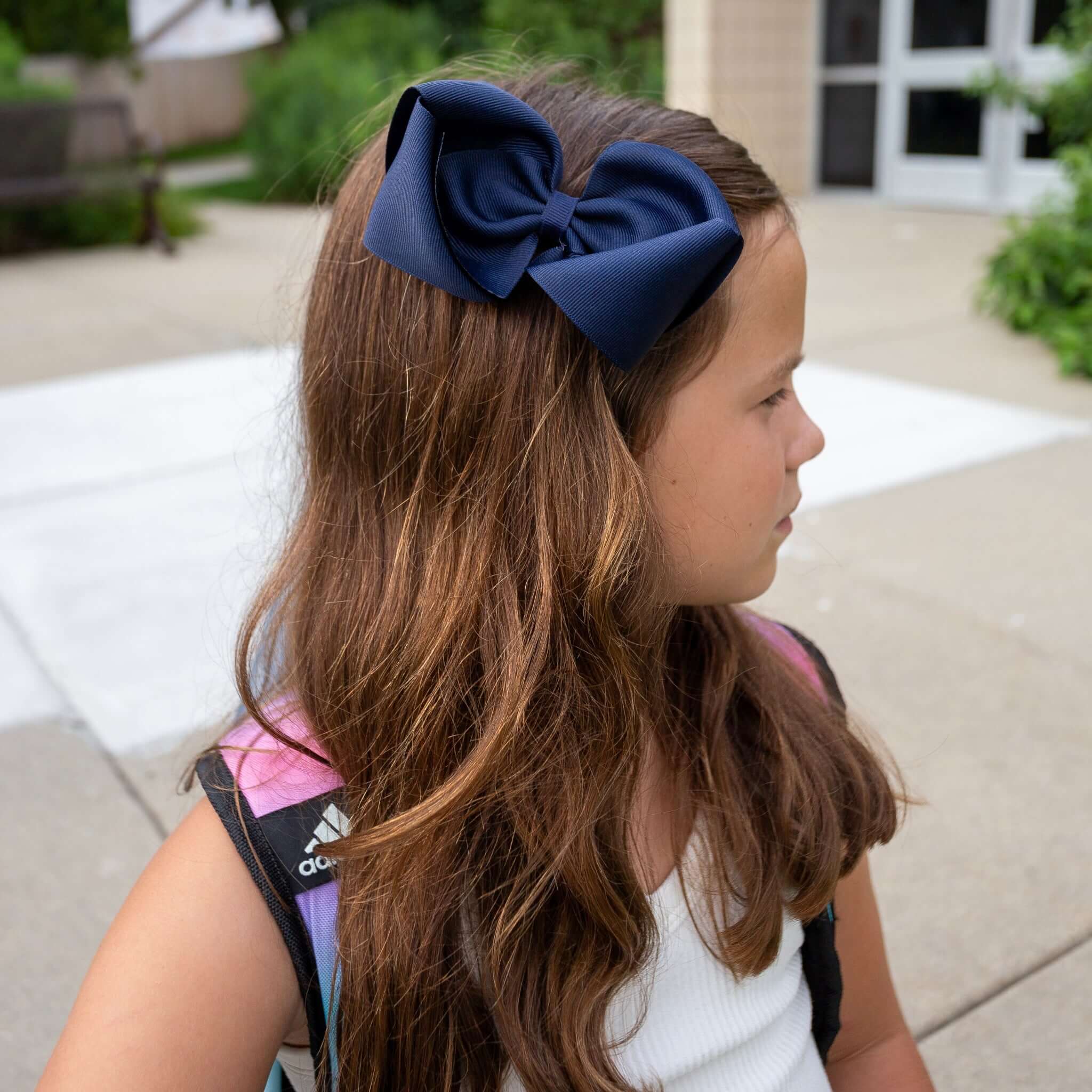 Youn girl  wearing 5 inch hair bow in navy in front of School.