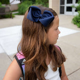 Youn girl  wearing 5 inch hair bow in navy in front of School.
