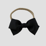 Black grosgrain Kayla hair bow on a nude nylon headband against a white background