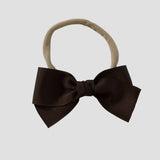 Brown hair bow on a nude nylon headband against a white background