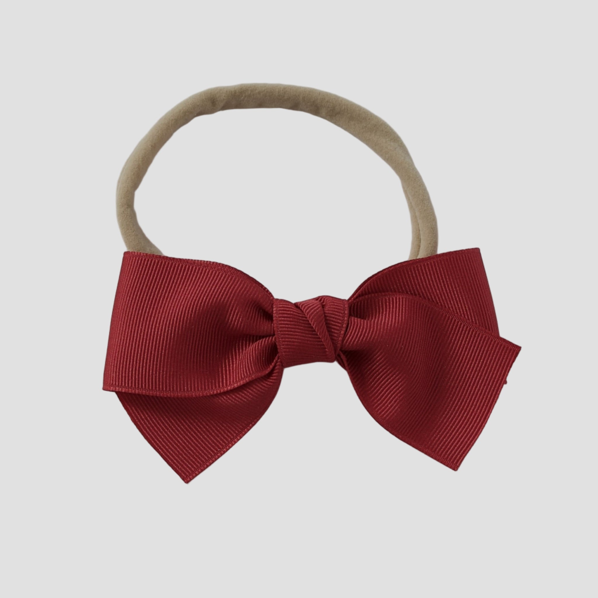 Cranberry red grosgrain Kayla bow on a nude nylon headband against a white background