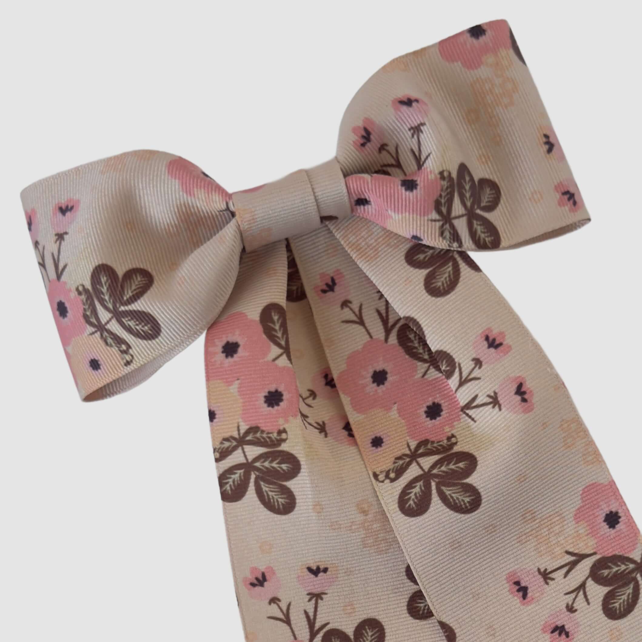 Elegant beige bow with a floral pattern featuring pink and brown flowers and leaves. The bow is symmetrical, conveying a soft, romantic tone.
