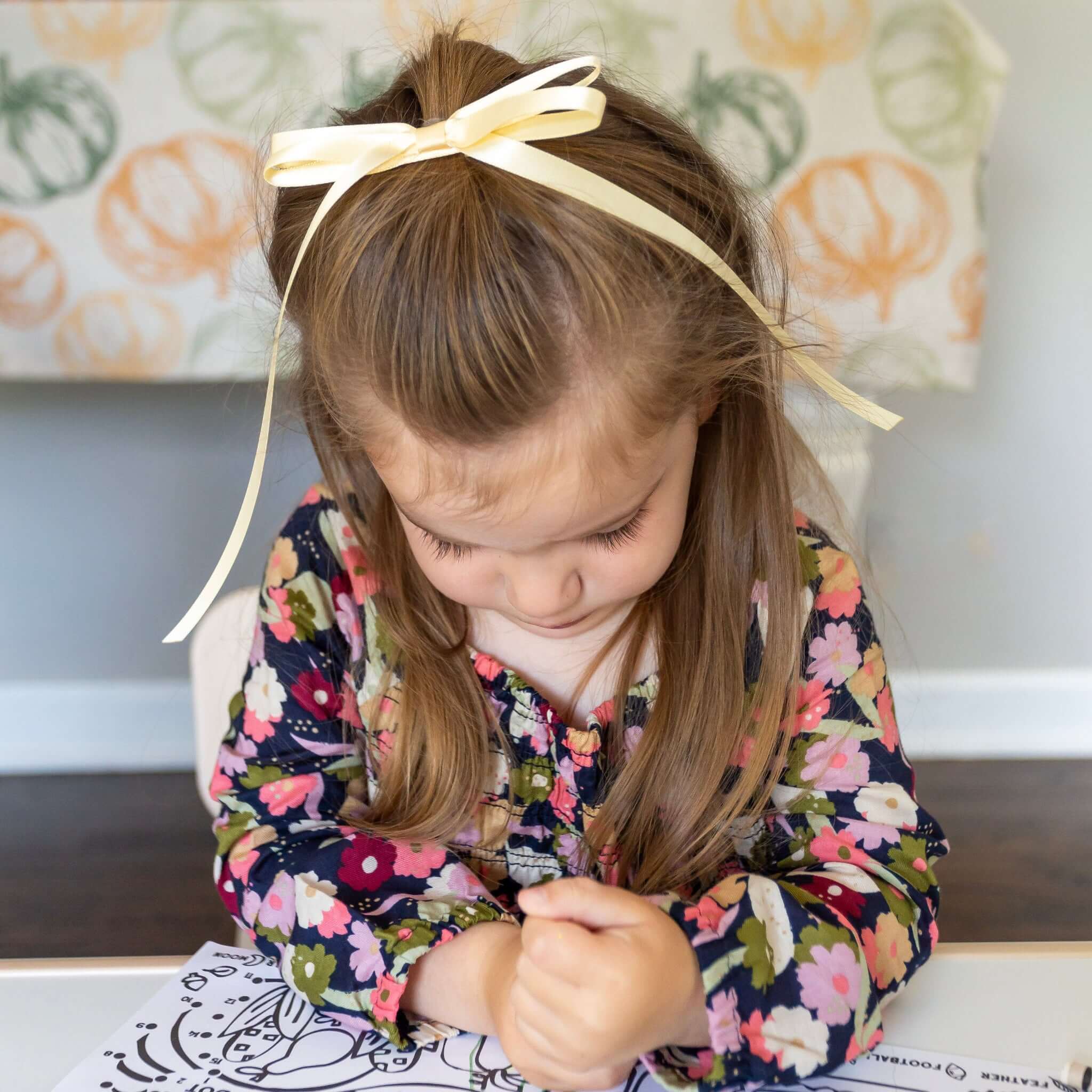 Young girl coloring at a table with a decorative headband wearing the Olivia satin bow in cream.