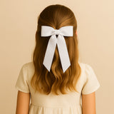 Girl with long hair wearing a large white grosgrain Zoe petite hair bow, against a beige background