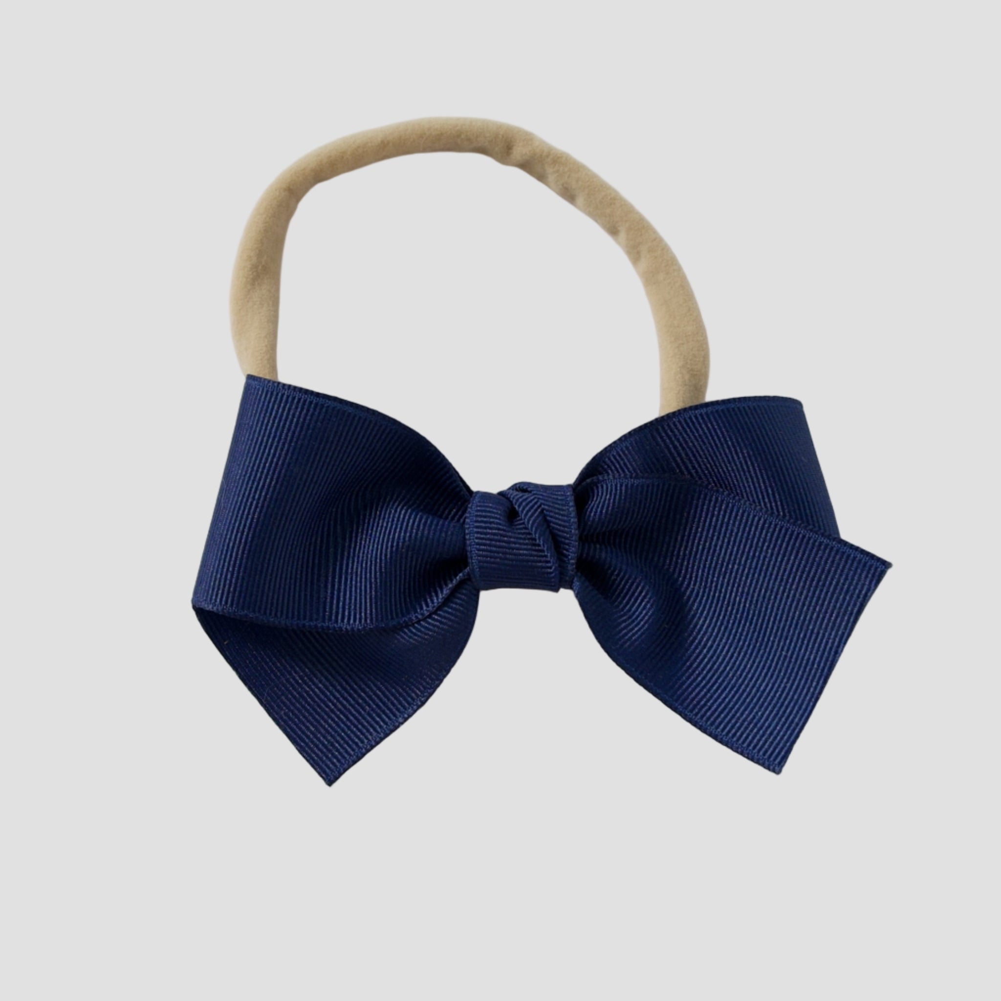 Light navy blue bow on a nude nylon headband against a white background