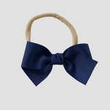 Light navy blue bow on a nude nylon headband against a white background