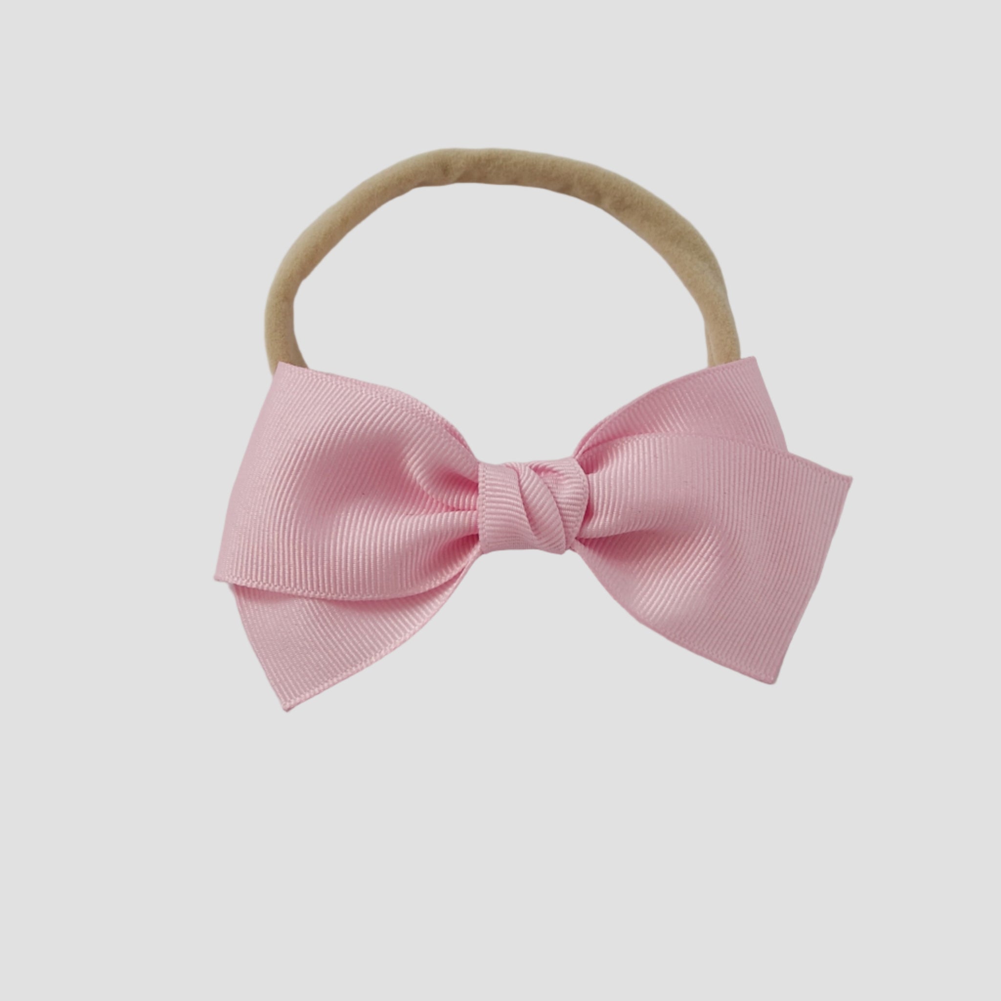 Light pink grosgrain Kayla hair bow on a nude nylon headband against a white background
