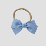 Blue grosgrain Kayla hair bow on a nude nylon headband against a white background