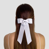 White hair bow on a person with long brown hair against a plain background