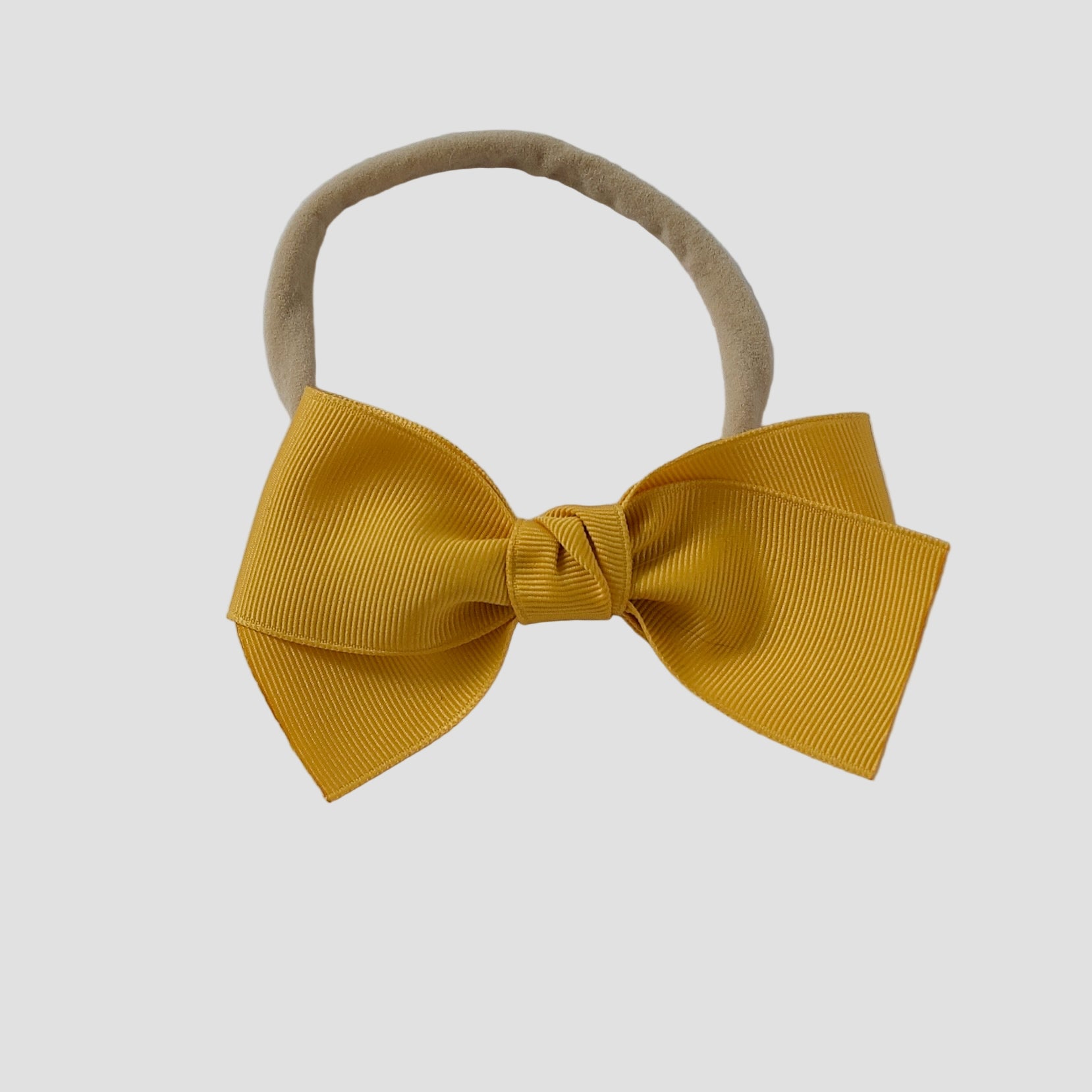 Mustard yellow grosgrain Kayla hair bow on a nude nylon headband against a white background