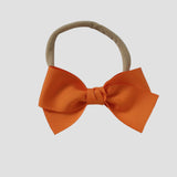 Orange grosgrain Kayla hair bow on a nude nylon headband against a white background