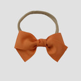 Pumpkin orange grosgrain Kayla hair bow on a nude nylon headband against a white background