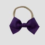 Purple grosgrain Kayla hair bow on a nude nylon headband against a white background