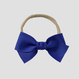 Royal blue grosgrain Kayla hair bow on a nude nylon headband against a white background