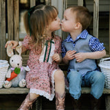 Two children, a girl and a boy, sitting on a wooden bench and kissing. Girl is wearing the Emerson satin bow in forest green.