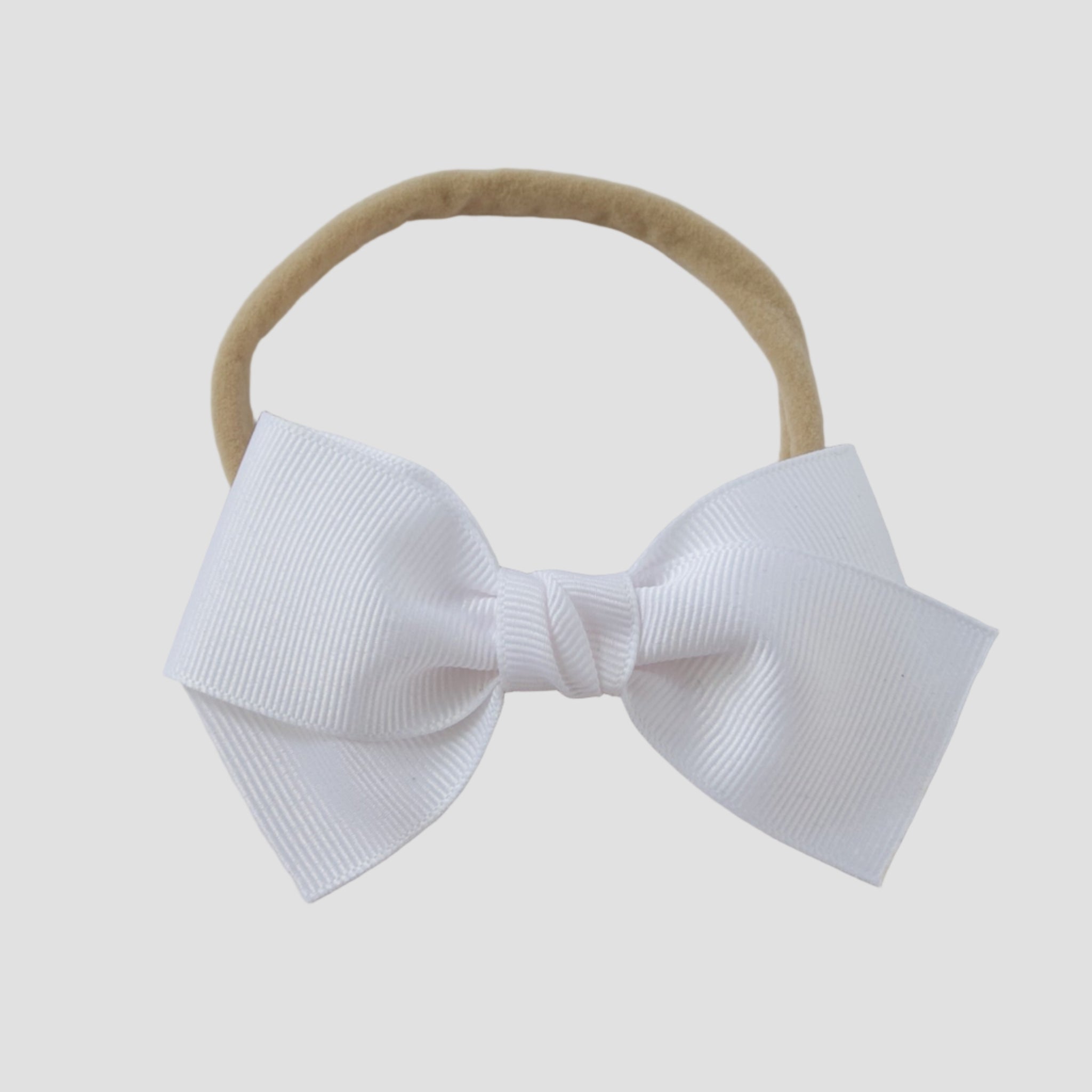 White grosgrain Kayla hair bow on a nude nylon headband against a white background