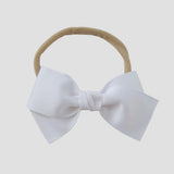 White grosgrain Kayla hair bow on a nude nylon headband against a white background