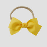 Yellow grosgrain Kayla hair bow on a nude nylon headband against a white background