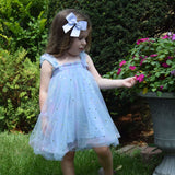Young girl in a light blue dress with a blue sailorbow standing in a garden.