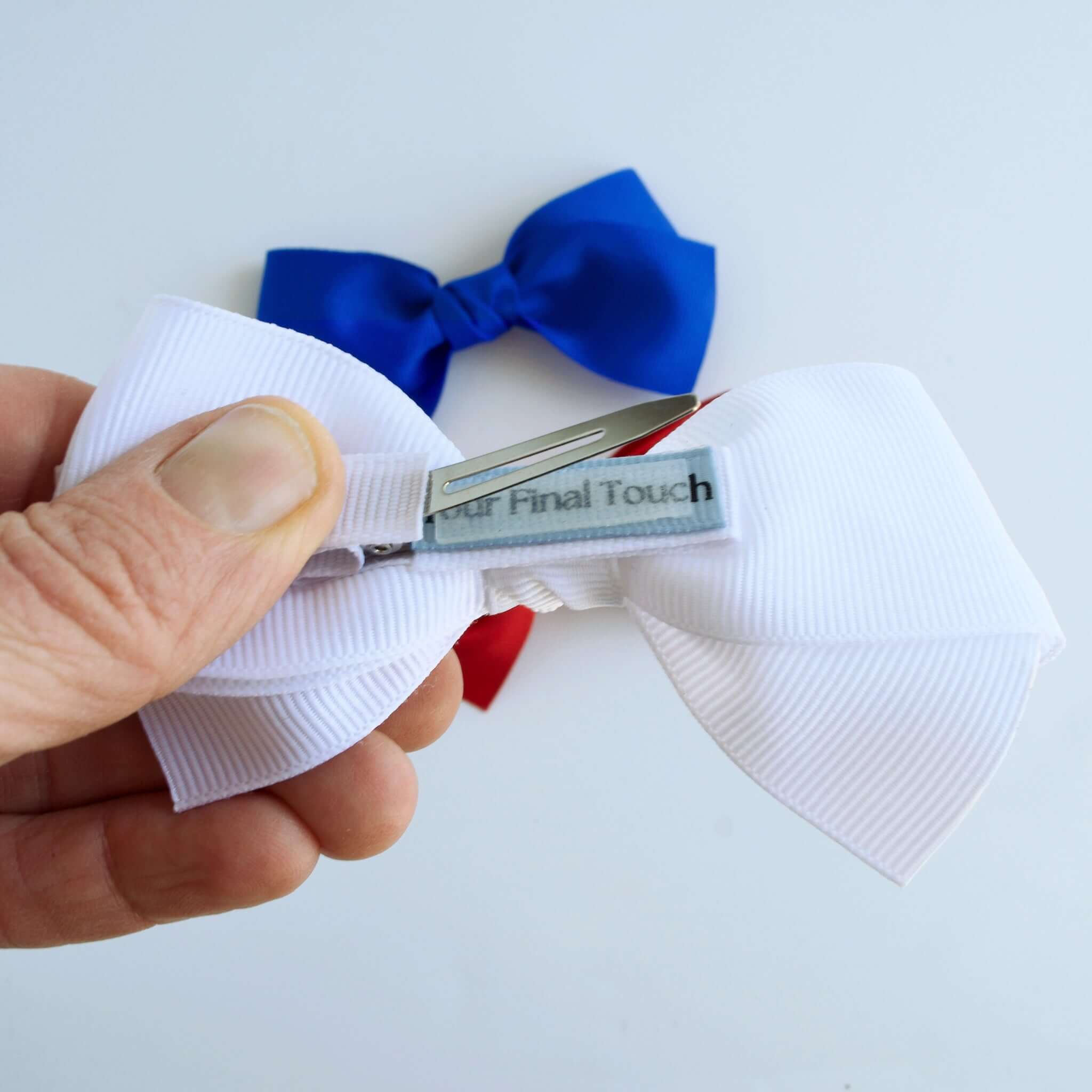 Close-up of white grosgrain hair bow with alligator clip and Your Final Touch label