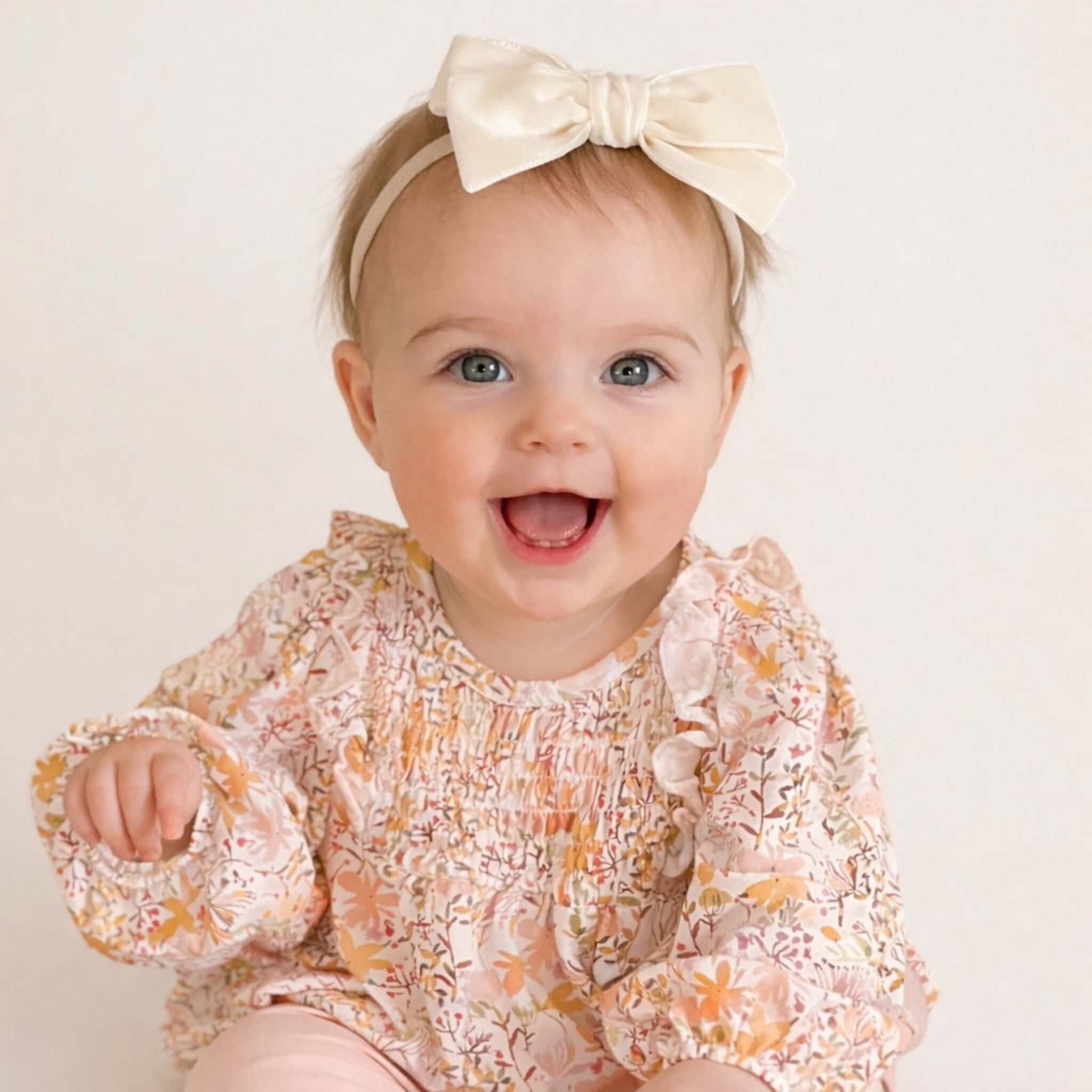 Baby wearing a floral outfit and ivory Kayla headband on a plain background