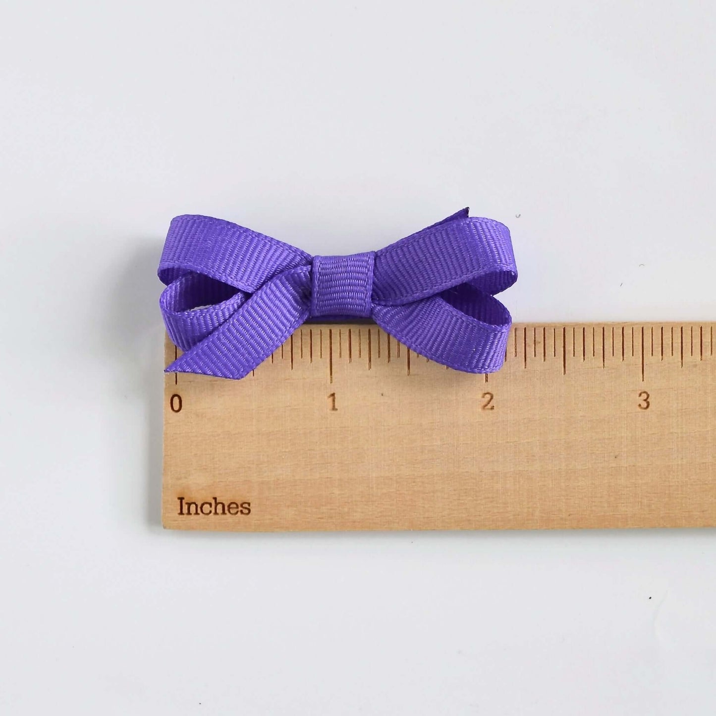 Purple grosgrain ribbon baby hair bow with snap clip and no slip grip, measured with ruler showing 1” W x 2.25” L