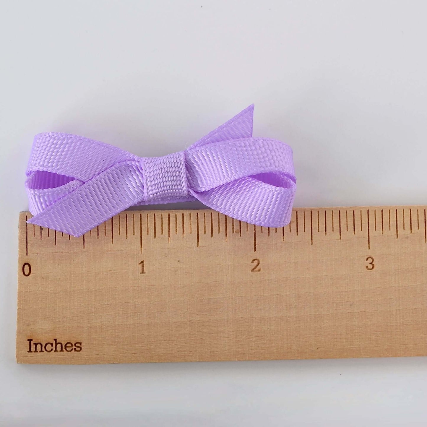 Mini grosgrain bow for babies and toddler girls on a ruler for size reference.