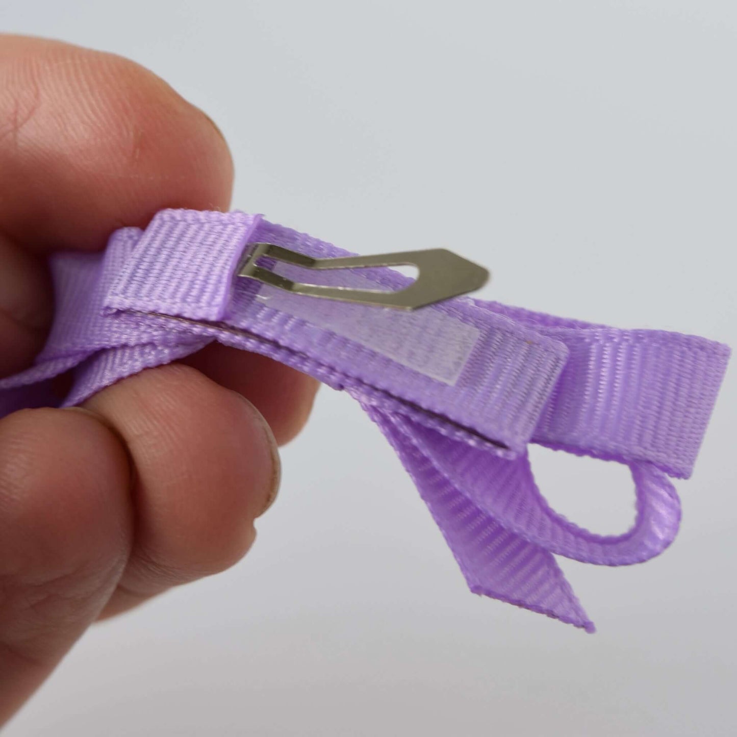 Close-up of a hand holding a mini grosgrain bow with a no-slip snap clip for babies and toddler girls.